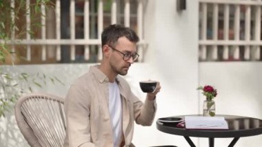 Genç bir iş adamı masaya oturur, kahve içer ve bir defterde çalışır. Bir arkadaş görür ve selamlaşmak için elini sallar..