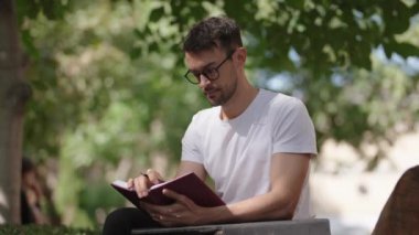 Adam parkta deftere yazı yazıyor. İlham, yeni fikirler ya da açık havada bir kitapla rahatlamak. Yavaş çekim videosu.