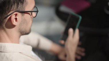 Açık kafede akıllı telefonunu kullanan bir adam. Telefonunu kontrol ediyor, mesaj atıyor, sosyal medyayı kullanıyor. Modern iletişim.