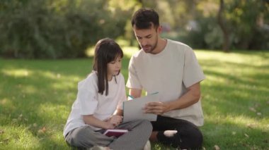 İlgili bir baba okul kızına parkta ev ödevlerinde yardım eder, aile bağlarını ve eğitimini destekler..