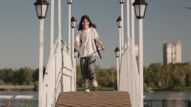 Neşeli genç bir kız okuldan sonra köprüden koşarak geçiyor, güneşin ve özgürlüğünün tadını çıkarıyor..