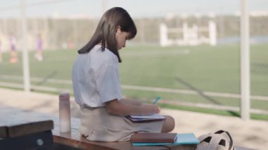 Genç kız okuldan sonra dışarıda ödev yapıyor. Liseli kız not defterine notlar yazıyor. Eğitim ve bilgi kavramı.