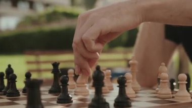 Açık havada oynanan bir satranç oyununun yakın çekimi. Sıcak güneş ışığı ve yeşil arka plan rahatlatıcı bir atmosfer yaratır..