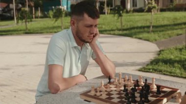 Eli çenesinde genç bir adam, parkta satranç oynarken derin düşüncelere dalmış..