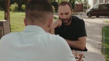 İki erkek arkadaş parkta birlikte satranç oynarken çok sıkı konsantre oluyorlar. İkisi de sonraki hamlelerini iyice düşünüyor..