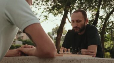 İki arkadaş parkta beton bir masada satranç oynuyor. Arkadaşı kararını beklerken bir adam hamlesini düşünüyor. Her ikisi de gündelik kıyafetler giyiyorlar..