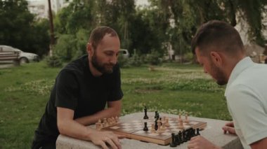 İki erkek arkadaş güneşli bir günde parkta satranç oynuyorlar. İkisi de kazanmaya odaklanmış ve kararlılar. Bu video strateji, arkadaşlık ve açık hava aktiviteleriyle ilgili..