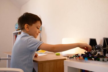 Genç bir çocuk sevinçle bir uzay gemisi modeli oluşturmaya odaklanıyor. Sahne, iyi organize edilmiş bir yatak odasında oyun sırasında yaratıcılık ve hayal gücünü yakalıyor.