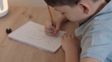 Genç bir çocuk bir masada oturuyor, bir defter çiziyor. Video çocukluk, yaratıcılık ve hayal gücünü çağrıştırıyor..