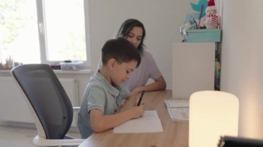 Bir annenin genç oğluna ev ödevinde yardım ettiği, olumlu bir öğrenme ortamı sağladığı ve ilişkilerini güçlendirdiği iç açıcı bir sahne..