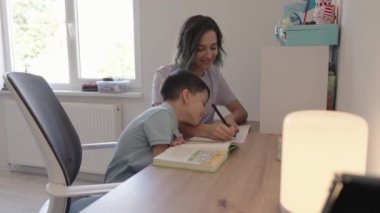 Bir anne oğluna ödevlerinde sevgiyle yardımcı olur, olumlu bir öğrenme ortamı oluşturur ve ilişkilerini güçlendirir..