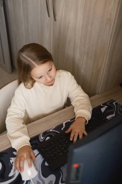 Bilgisayar faresi ve klavyesinde gezinen genç bir kız ev ortamında dijital teknolojiyi keşfediyor..