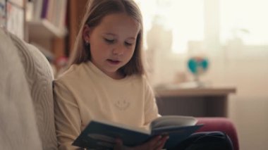 Oturma odasındaki bir kanepede rahat bir şekilde oturan genç bir kız büyüleyici bir kitap okumaya dalmış, huzurlu bir öğleden sonranın tadını çıkarıyor..