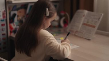 Genç bir kız masasında oturuyor ve bir deftere yazıyor. Odaklanmış ve işine odaklanmış durumda..