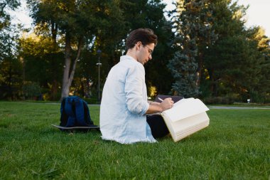 Eskiz defteriyle çimlerin üzerinde oturan düşünceli bir birey, parkın dinginliğinin tadını çıkarıyor. Kurulum, yaratıcılığı vurgulayan doğal unsurlara ve rahat bir açık hava yaşam tarzına sahiptir..