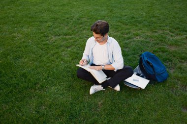 Sırt çantası ve defteriyle çimenlerde okuyan bir adam öğrenirken doğanın tadını çıkarıyor..