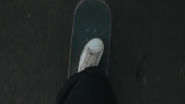 Boş bir yolda giden bir kaykaycının bakış açısı. Kaykaydaki beyaz ayakkabıların yavaş çekim görüntüleri. POV şehir sokak pateni.