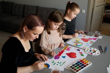 Bir anne ve iki kızı rahat bir ev ortamında yaratıcı resimlerin keyfini çıkarıyorlar. Yaratıcılığını, aile bağını ve sanatsal ifadesini canlı suluboya ve takım çalışması ile gösterir.