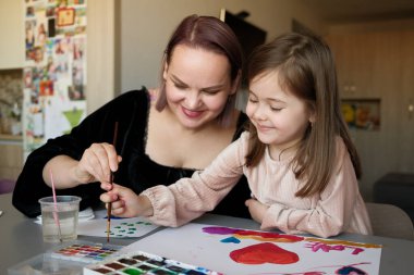 Bir anne ve kızı rahat bir ev ortamında birlikte resim yapmaktan hoşlanırlar. Yaratıcılıkla bağ kurarlar, gülümseme ve neşe paylaşırlar ve suluboya resimlerle kağıt üzerinde renkli sanat eserleri yaratırlar..