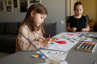 İki çocuk suluboya ile yaratıcı bir resim aktivitesi içinde, sanatsal keşifler ve yaratıcılık sergiliyorlar. Sahne sade, çocukluk sevincinin ve eğlencenin sanat ve oyun yoluyla vurgulandığı bir yer..