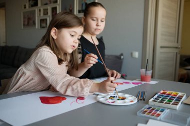 İki genç kız yaratıcı aktiviteler yapıyor, rahat bir ev ortamında suluboya ile resim yapıyorlar, yaratıcılığı ve eğlenceyi teşvik ediyorlar..