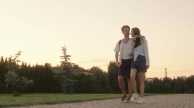 Gün batımında parkta yürüyen romantik aşık genç bir çift. Barışçıl bir akşamın tadını çıkarırken birbirlerini kucaklıyorlar..