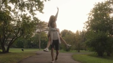 Parkta eğlenen genç bir çiftin romantik videosu. Adam kadını sırtında taşıyor. Hem gülüyor hem de gülüyor..