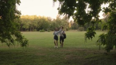 Romantik bir çift yaz günü parkta el ele yürüyorlar. Erkek, ağaçların arasından yürürken kolunu kadının omzuna atar..