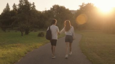 El ele tutuşan genç bir çiftle romantik bir akşam yürüyüşü. Parktaki batan güneşe doğru kameradan uzaklaşmak. Romantik, aşk, ilişki hedefleri.