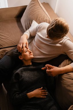 Sevgi dolu bir çift rahat bir ev ortamında rahat bir kanepede birlikte vakit geçirmenin tadını çıkarıyor. Duygusal bağlantıları ve rahat tavırları derin ve sıcak bir atmosfer yaratıyor..