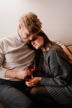 Kanepede dinlenen, sıcak bir ortamda kırmızı şarap içen bir çift. Yakın ve sevecen görünürler, anı samimi, samimi, sevgi ve rahatlık dolu hissettirirler..