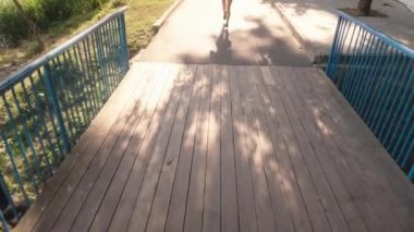 Genç bir kadın köprüden geçiyor. Spor kıyafetleri ve koşu ayakkabıları giyiyor. Kameraya doğru koşarken kamera ayaklarına bakıyor..