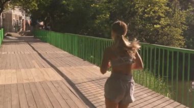 Genç bir kadın yaz günü yeşil bir şehir parkında koşuya çıkar..