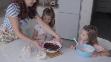 Annem iki küçük kızının mutfakta çikolatalı tatlı pişirmesine yardım ediyor. İçindekileri hazırlarken gülümsüyor ve gülüyorlar..