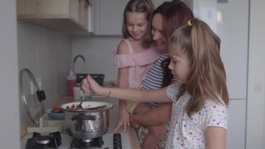 Bir anne ve iki kızının mutfakta yemek pişirirken eğlendikleri yürek ısıtan bir sahne. Aile mutlu mesut birlikte yemek hazırlıyor, güzel anılar yaratıyor..