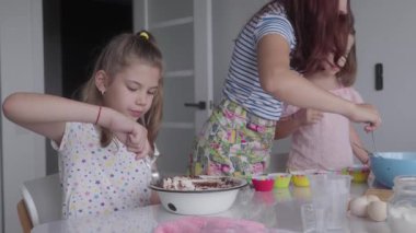 Mutfakta birlikte kek pişiren mutlu bir aile. Bir anne ve iki kızı bir kasede malzemeleri karıştırıyorlar. Aile yemek yaparken gülümsüyor ve gülüyor..