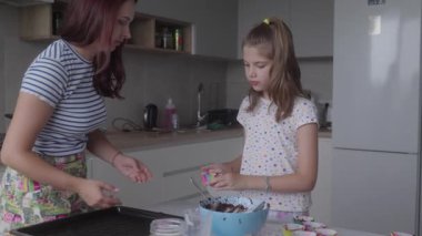 Bir anne ve küçük kızı mutfaklarında birlikte yemek pişiriyorlar. Kek yapıyorlar ve çok eğleniyorlar. Sahne çok iç açıcı ve ebeveyn ile çocuk arasındaki bağı gösteriyor..