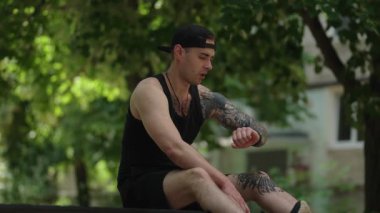 Formda bir genç adam parkta bir bankta oturuyor. Antrenmanına ara verip akıllı kasetindeki fitness izleyicisini kontrol ediyor..