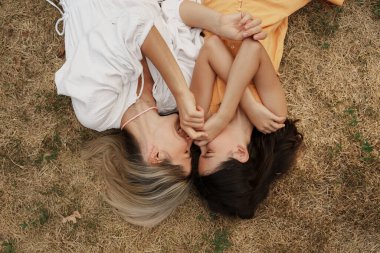 Anne ve kızı çimenlerde uzanıp neşeli ve eğlenceli bir anı paylaşıyorlar..