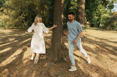 Güneşli bir parkta ağacın etrafında kovalamaca oynayan iki arkadaş..