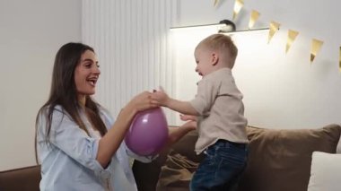 Anne ve oğlu evlerindeki kanepede bir balonla oynuyorlar..