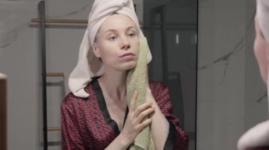 Kafasında havlu olan bir kadın banyoda duş aldıktan sonra yüzünü bir bezle kurutuyor..