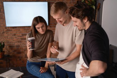 Tuğla duvarlı bir çalışma alanında tablet kullanarak bir projede işbirliği yapan üç iş arkadaşı.