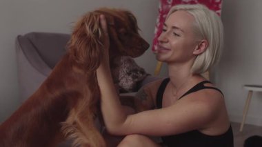 Sarışın bir kadın Cocker Spaniel köpeğine gülümsüyor. Evdeler ve birlikte vakit geçiriyorlar. Sahibi yerde oturup onu okşarken köpek ayağa kalkar..