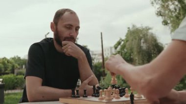 İki erkek arkadaş bulutlu bir yaz gününde parkta bir bankta satranç oynuyorlar. Bir arkadaşım bir sonraki hamlesini düşünüyor..