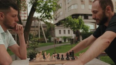 İki arkadaş parkta stratejik bir satranç oyunu oynuyor. Bir sonraki hamlelerine konsantre oluyorlar..