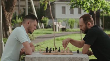 İki erkek arkadaş park masasında satranç oynarken sıkı bir şekilde konsantre oluyorlar. Birlikte boş zamanlarının tadını çıkarırken, her ikisi de stratejik düşünüyor..