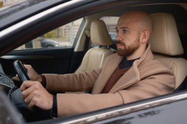 Bej ceketli bir adam lüks bir araba sürerken odaklanır..