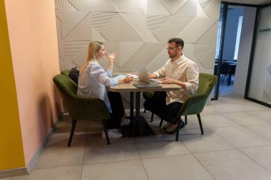 Profesyonel meslektaşlar, hafif ofis ortamında dizüstü bilgisayarlarla tartışıyorlar.