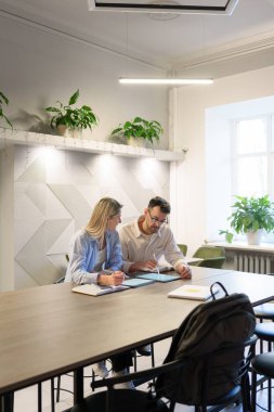 İki profesyonel, iyi aydınlatılmış bir ofiste tablet üzerinde birlikte çalışıyorlar.